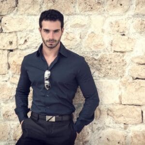 A man in black shirt and pants leaning on wall.